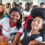 Mulher sorrindo sentada ao lado de rapaz jovem e sorridente sentado numa cadeira de rodas.